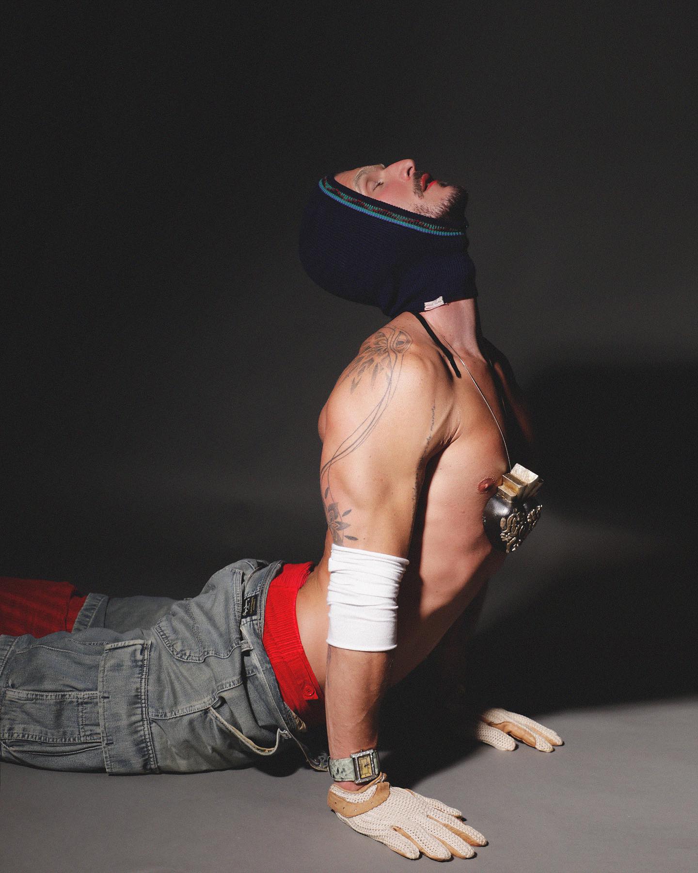 Alex Trevelin reclinado com capuz de tricô, luvas e styling de Michael Juvêncio