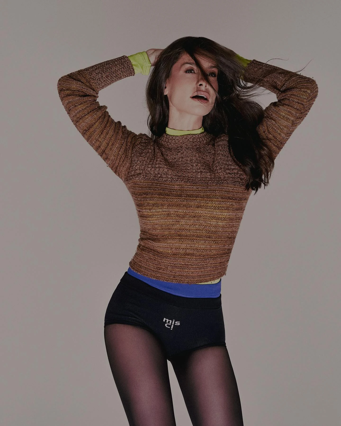 Alinne Moraes em tricô marrom com gola e punhos verde-limão e hot pant preta