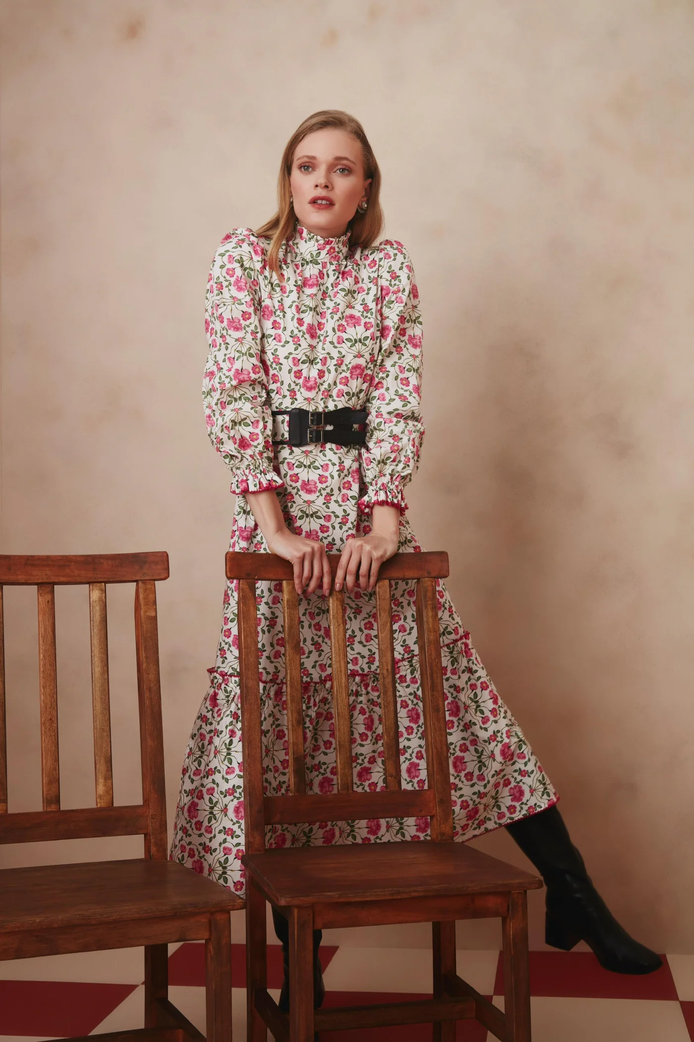 Thais Custodio em vestido floral rosa atrás de cadeiras de madeira