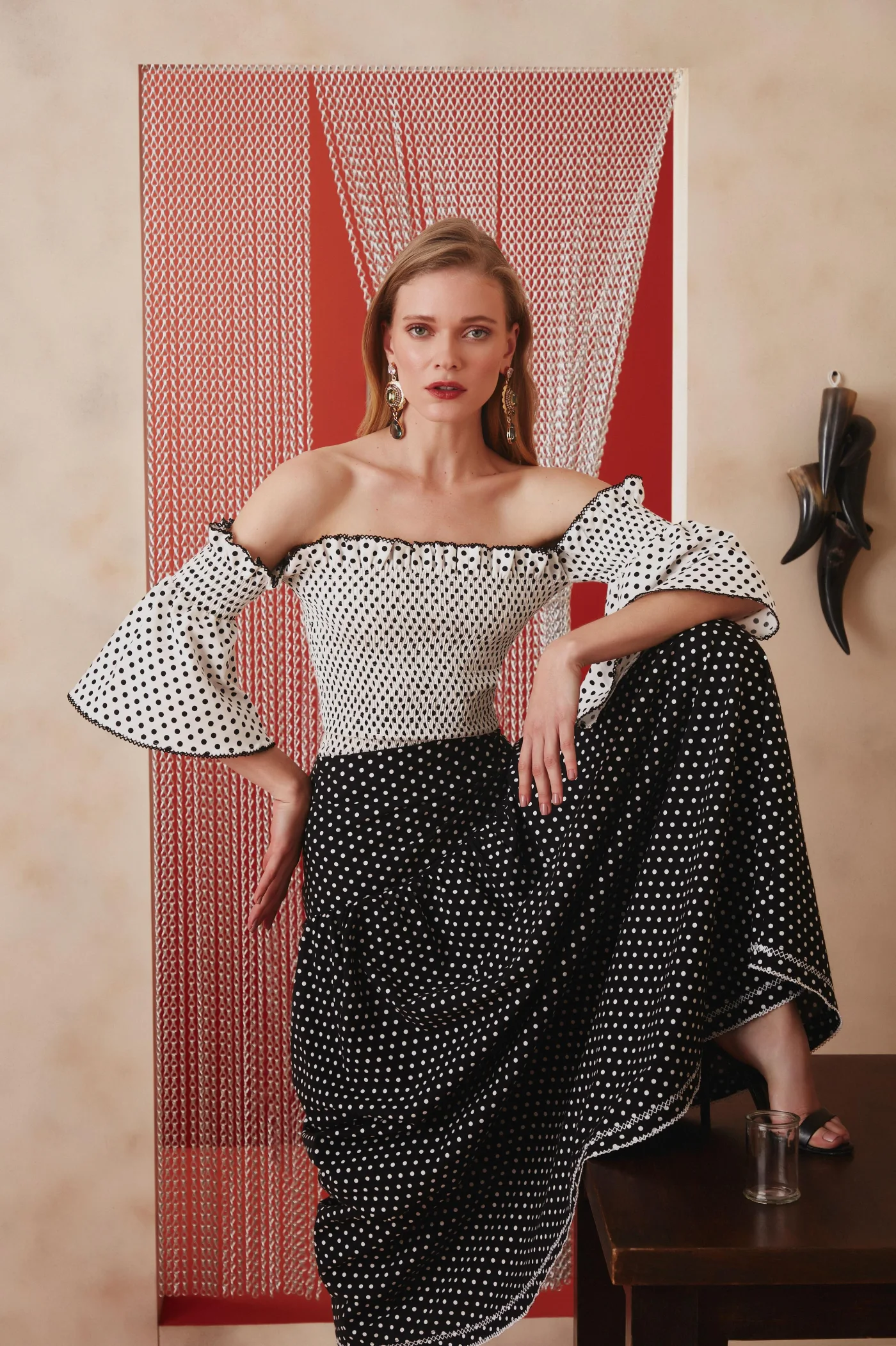 Thais Custodio em look preto e branco de poás diante de cortina de correntes