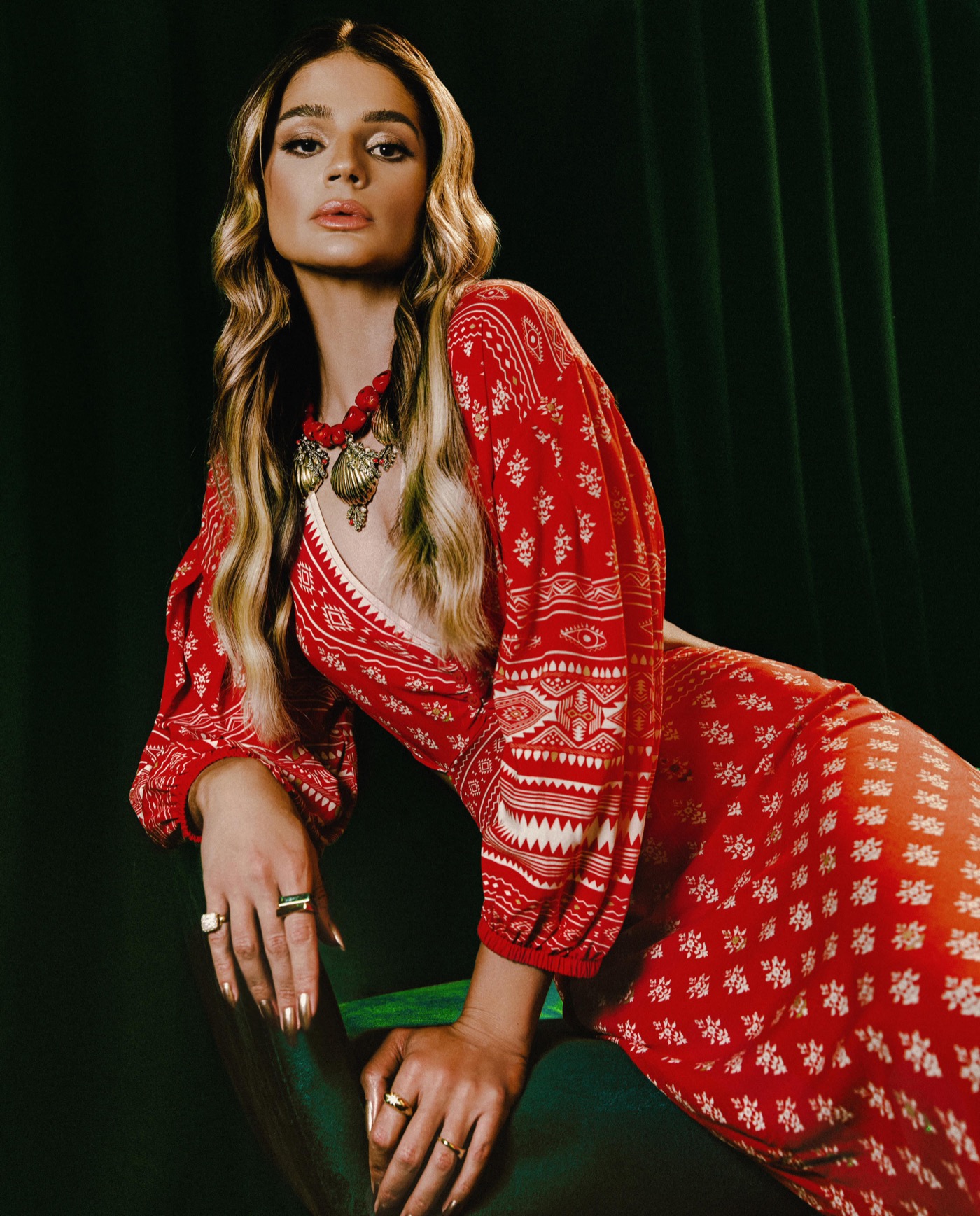 Retrato de Thássia Naves em vestido vermelho Colcci com acessórios dourados